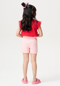 Rød kortærmet top med flæser i kanterne, parret med lyserøde shorts med elastisk talje og kontrastkant; pink sko.