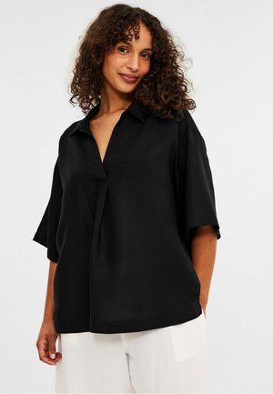 Black short-sleeve button-up shirt with a collar and V-neckline, featuring a relaxed fit and smooth texture. Paired with light-colored pants.
