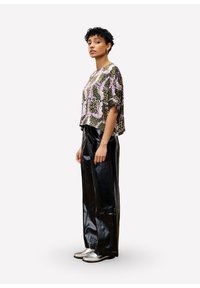 Korte mouw top met een abstract patroon in paars, groen en zwart, gecombineerd met glanzende zwarte wijdpijpsbroeken en zilveren schoenen.
