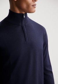 Pullover blu navy con zip al collo, realizzato in morbido tessuto knit. Presenta un colletto alto e una zip di mezza lunghezza sul collo.