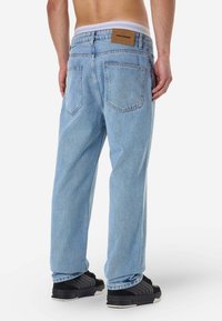 Απαλές μπλε τζην παντελόνες με ίσια εφαρμογή, διαθέτοντας μια δερμάτινη ετικέτα στην πλάτη, δύο πίσω τσέπες και ελάχιστες λεπτομέρειες ραφής.