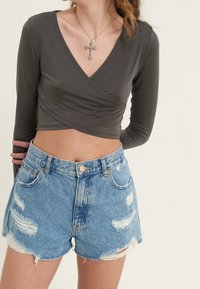 Dunkelgraues langärmeliges Wickeloberteil kombiniert mit verblichenen hellblauen Denim-Shorts mit fransigen Kanten und hohem Bund.