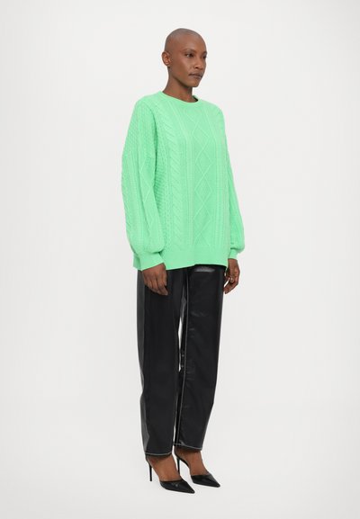 Maglione in maglia a coste di colore verde neon, dalla vestibilità ampia, con polsini e orlo a coste, abbinato a pantaloni in pelle nera lucida e décolleté nere a punta.