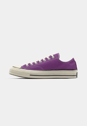 Purple canvas sneaker with white laces, rubber toe cap, and a cream-colored sole featuring black stripes. Low-top design, rounded shape.