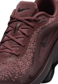 Sneaker Nike w kolorze bordowym, z chropowatym materiałem, czarnymi akcentami, wiązanym designem i wyściełaną podeszwą. Charakterystyczny wzór siatki na cholewce.