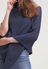 Mörkblå stickad tröja i en avslappnad passform, med vida ärmar och strukturerat mönster, i kombination med ljusblå denimjeans.