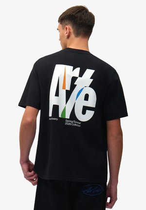 Uomo che indossa una t-shirt nera con grande scritta stilizzata "Arté" e accenti colorati, "Collezione Primavera/Estate 2026" stampata sul retro.