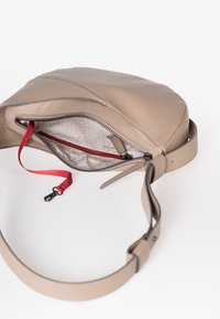 Lichtbruine leren schoudertas met een open rits, die de geruite voering, een interne ritszak en een rode stoffen sleutellabel met klikfunctie toont.