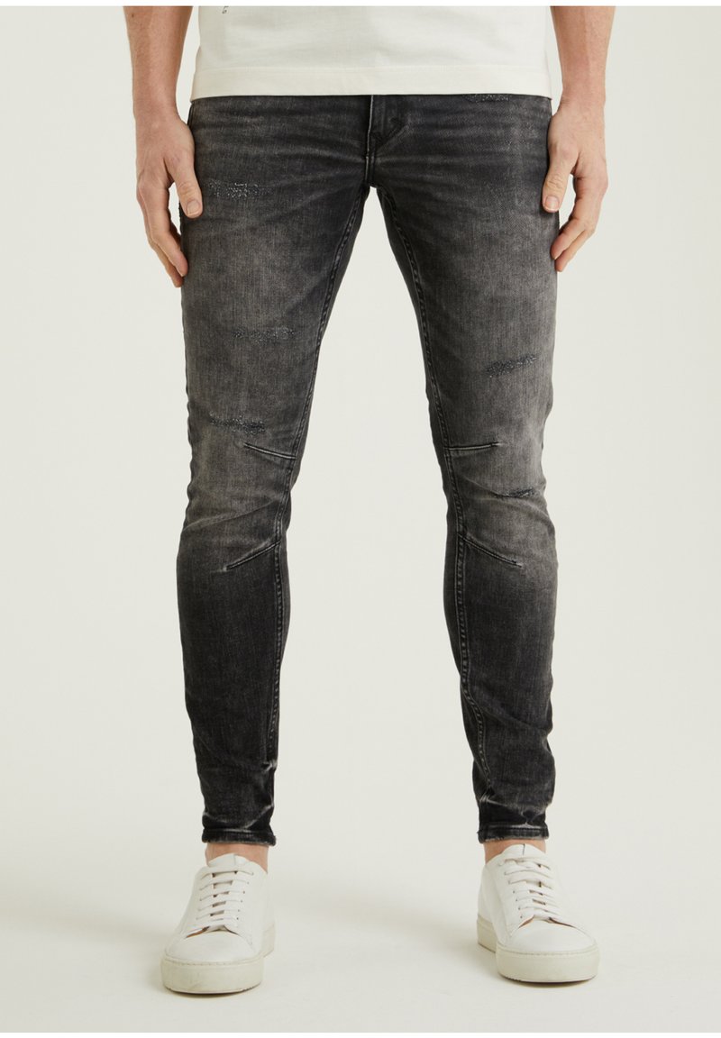 Vaqueros de mezclilla negros con un ajuste slim, que presentan detalles desgastados y un lavado descolorido. Combinados con zapatillas blancas para crear contraste.