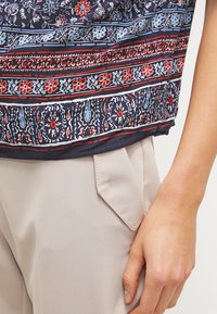 Yhdenmukaisella meripaidalla, jossa on punaisia ja sinisiä kukkakuvioita, lyhyet hihat ja rento istuvuus, yhdistettynä vaaleanbeigeihin housuihin, joissa on sivutaskut.