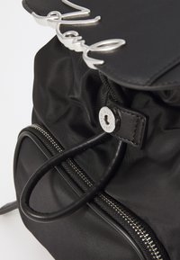 Black nylon backpack with a smooth texture, featuring silver hardware, a zip closure, and a prominent loop detail on the flap.