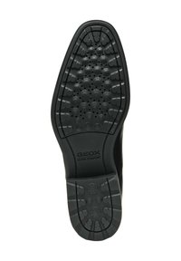 Suela de zapato de goma negra con patrón de dibujo circular, que presenta una textura en relieve y pequeños agujeros de ventilación. Marcada con "GEOX ULTRA COMFORT".