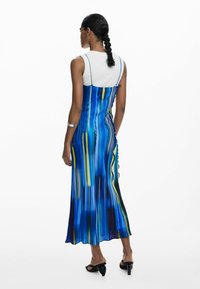 Rochie cu dungi albastre și galbene, cu bretele ajustabile și o siluetă fluidă, asortată cu un top alb și sandale cu toc negre.