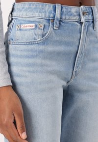 Jeans in denim blu chiaro con una vestibilità classica. Presentano un'etichetta Calvin Klein sulla tasca posteriore, chiusura con bottone e una leggera sfumatura.