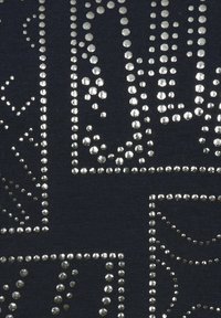 Donkere stof met metalen studs die zijn gerangschikt in geometrische patronen, wat zorgt voor afwisselende texturen en visuele interesse over het oppervlak.