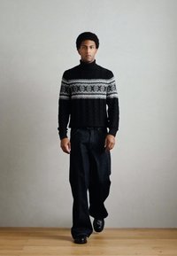Čierny pletený sveter s vysokým golierom, zdobený svetlým fair isle vzorom. Kombinovaný s voľnými tmavými džínsami a čiernymi topánkami.