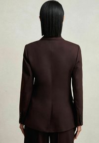 Blazer marron ajusté avec un design structuré, des revers aigus et des manches longues. Il présente une fente simple à l'arrière et des accents de poignet boutonné.