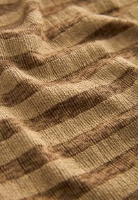 Struktureret stof med skiftende beige og brune striber, der fremviser et vævet design. Overfladen ser blød ud og er let forhøjet.