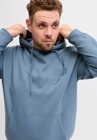 Ανοιχτό μπλε φούτερ με κουκούλα, τσέπη μπροστά, κορδόνι στη κουκούλα και διακριτικό λογότυπο στο ύφασμα. Ομαλή υφή και άνετη εφαρμογή.