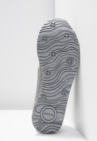 Zool van een grijze schoen met golvende profielpatronen en ronde gripvlakken, merknaam "WODEN" zichtbaar nabij de hiel.