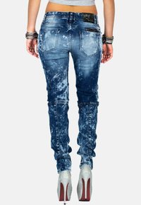 Jeans skinny in denim blu sbiadito con dettagli strappati, caratterizzati da una vita alta e tasche posteriori. Abbinati a tacchi alti argentati.