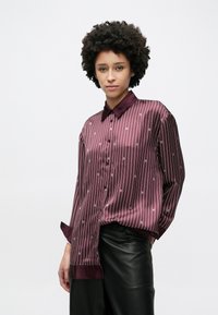 Burgundská saténová košile s vertikálními bílými pruhy a jemnými detaily loga, vybavená klasickým límcem a dlouhými rukávy.