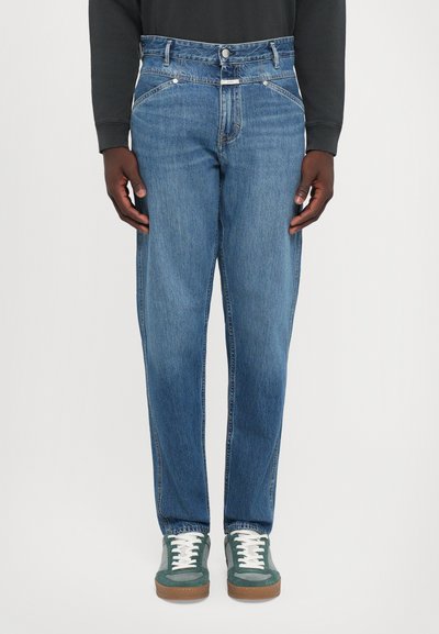 Lichtblauwe denim jeans met een slim fit, vijf-pocket ontwerp en subtiele stiksels. Gecombineerd met groene sneakers en witte veters.