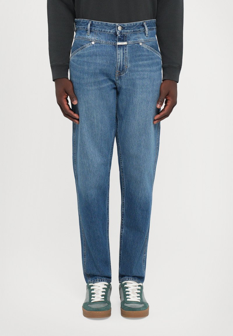 Jeans din denim de culoare albastră deschisă, cu croi slim, design cu cinci buzunare și detalii de cusătură subtile. Asortați cu adidași verzi și șireturi albe.