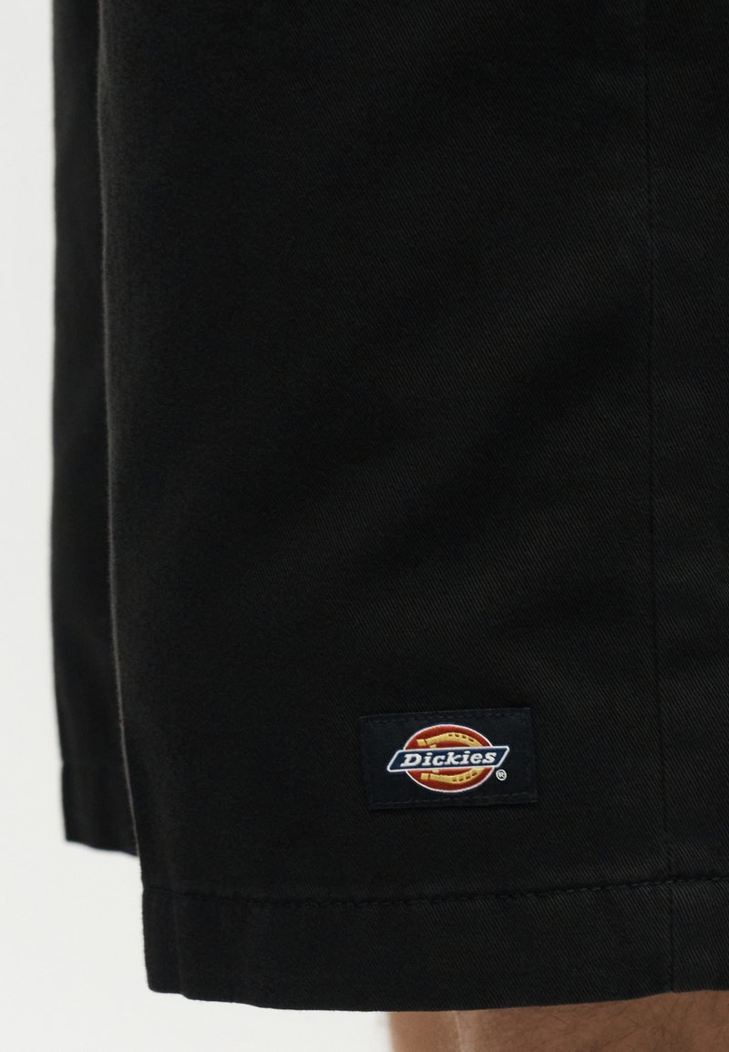 Gros plan sur un short en tissu noir avec un petit logo rectangulaire Dickies près de l'ourlet.