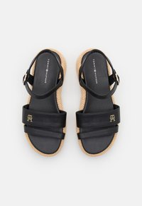 Black leather sandals with two wide straps and a logo. The sole features a woven, natural texture, and an adjustable ankle strap.