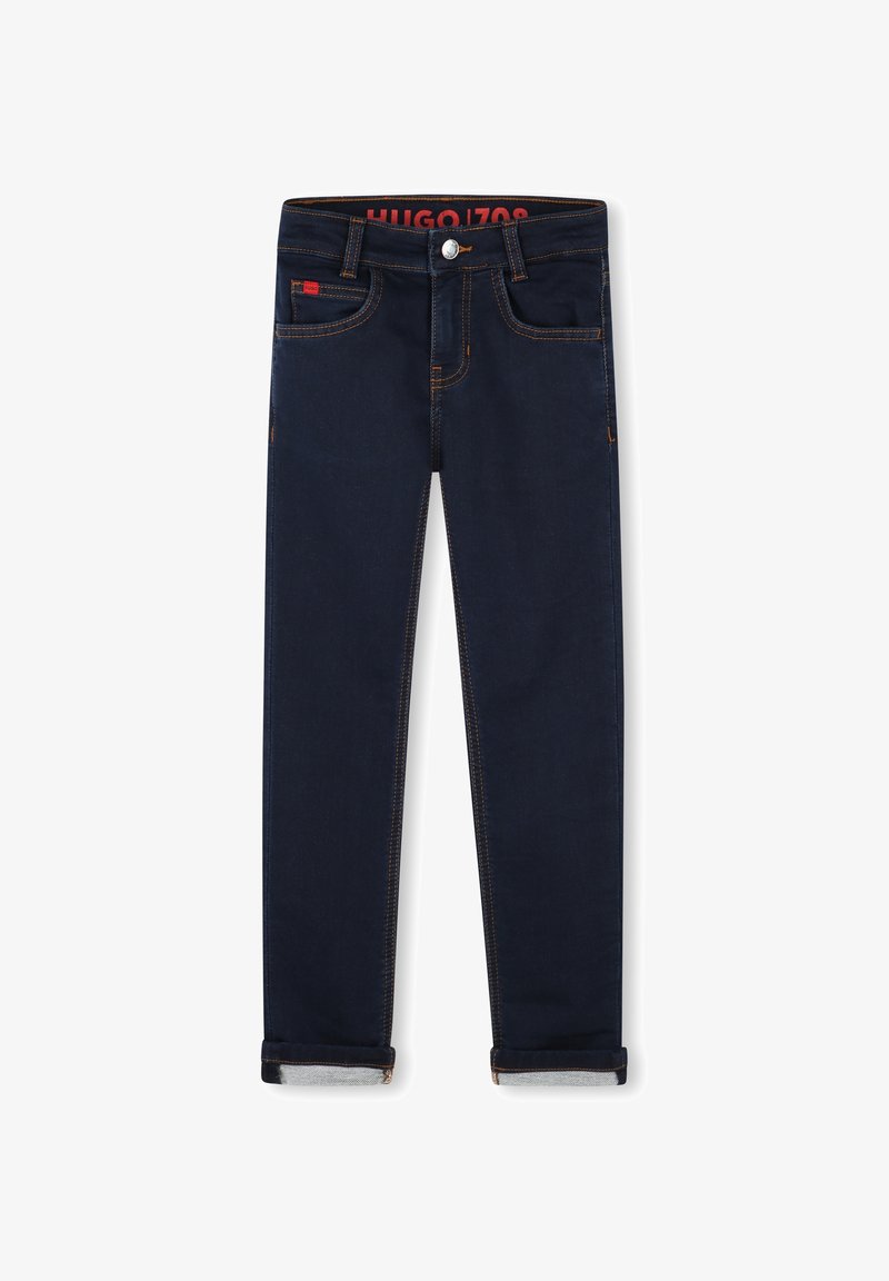 Jean en denim bleu foncé, doté de cinq poches, de coutures contrastantes orange et d'un ourlet roulé aux chevilles. Logo de la marque sur la taille.