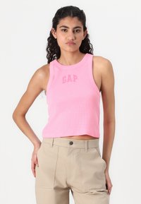 Rožinė trumpa maikutė su apvali iškirpte ir šviesiai rožiniu "GAP" logotipu. Pagaminta iš raukšlėto audinio. Sujungta su smėlio spalvos kelnėmis, kurios turi laisvą siluetą.