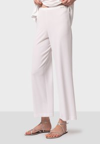 Pantalons larges blancs en tissu léger, avec une texture lisse et un léger éclat. Associés à des sandales à lanières argentées.