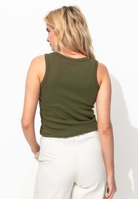 Débardeur côtelé vert olive avec un col rond, coupe ajustée et sans manches, associé à un pantalon écru.