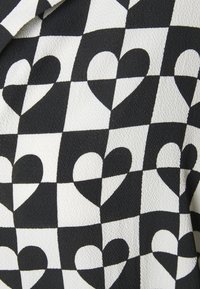 Tissu noir et blanc présentant un motif en damier avec des cœurs ; la surface texturée ajoute de la profondeur, créant un intérêt visuel.