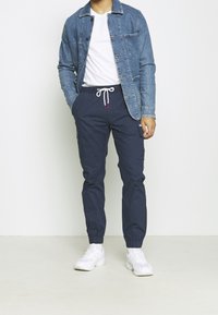 Světle modrá džínová bunda, bílé tričko a tmavě modré námořnické kalhoty s elastickými manžetami; kalhoty mají stahovací pás a červený akcent. Bílé tenisky.