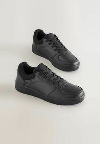 Baskets noires au design bas, en cuir, avec une surface texturée, dotées d'un système de laçage à l'avant et d'une semelle en caoutchouc. Pas de logos visibles.