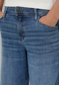 Niebieskie dżinsy z denimu o średnim stanie, z zapięciem na guziki, pięcioma kieszeniami i subtelnym wyblaknięciem oraz gładką fakturą.