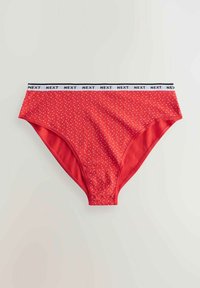 Röda bomullsbriefs med vita prickar och ett svart band märkt "NEXT." Har en slät textur och klassisk skärning.