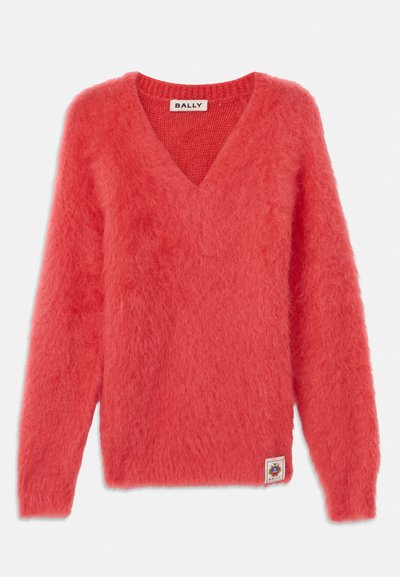 Coral pink v-neck sweater with loose, fuzzy texture; long sleeves; ribbed neckline; features a side brand patch with logo.
