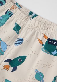Beige Shorts mit elastischem Bund, die ein Muster aus Raketen und Planeten in Grün-, Blau- und Grautönen aufweisen, mit einem kleinen Logetikett.