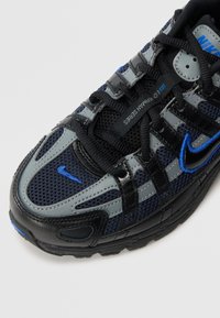 Baskets Nike en noir, gris et bleu ; caractéristiques en maille et matériaux synthétiques, motifs texturés, système de laçage et un logo distinct.
