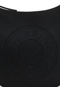 Sac en cuir noir présentant un design perforé circulaire avec le mot "KARL" au centre. Texture lisse avec une fermeture éclair.