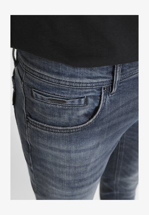 Jeans de mezclilla azul oscuro con una textura desgastada, que cuentan con un bolsillo delantero y bolsillos traseros, acentuados con costuras y herrajes en negro.