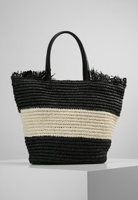 Sac fourre-tout tissé présentant des rayures alternées noires et crème, fabriqué à partir de fibres naturelles, avec deux poignées robustes et une finition texturée.