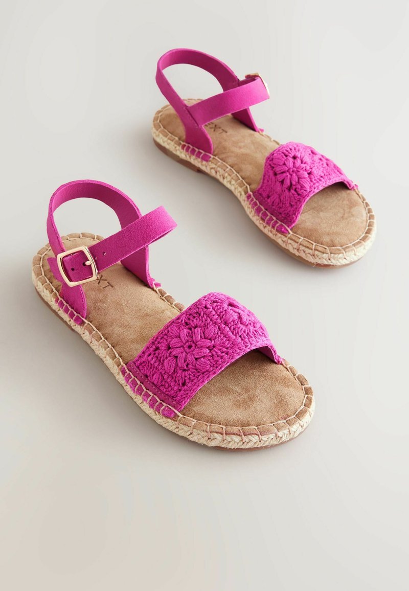 Rosa sandaler med ett virkade ovandel och en platt espadrillesula. Har ett framrem och en ankelrem med detaljer i silverfärg.