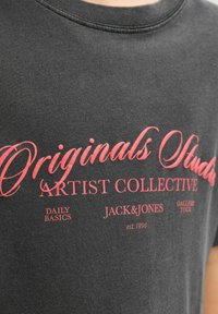 Camisa gris oscuro con texto rojo que dice "Colección de Artistas Originales del Estudio", "Básicos Diarios", "Jack & Jones" y "Gira de Galerías est. 1990."