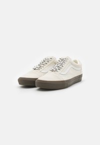 White canvas sneakers with textured upper, grey rubber sole, and metallic lace accents. Classic low-profile design.