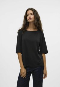 Top negro de manga corta y escote ancho, con una textura suave hecha de tejido ligero. Combinado con jeans oscuros.