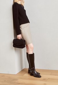 Zwarte gebreide trui, beige midi-jurk en kniehoge zwarte leren laarzen. Houdt een gestructureerde zwarte handtas met een klep-sluiting vast.